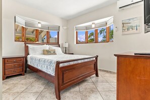 A bedroom with a wooden bed, a nightstand, a dresser, and a window with a view of palm trees. - Bubali Villa - Just a 2-minute drive to Eagle Beach (Eagle Beach)