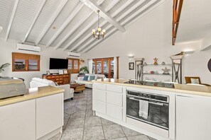 A spacious kitchen with a central island, a dining area with a white table and chairs, and a living room with a sofa and a television.