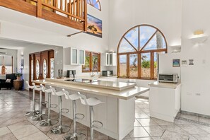 A spacious kitchen with a central island, bar stools, and a large window offering a view of the outdoors.