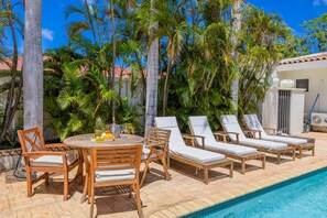 Un espace aménagé au bord de la piscine, avec des chaises longues, une table garnie de fruits et de boissons, et une piscine à l’eau d’un bleu limpide.