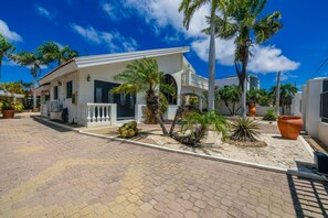 A modern two-story house with a covered porch, surrounded by palm trees and potted plants. - Bubali Villa - Just a 2-minute drive to Eagle Beach (Eagle Beach)
