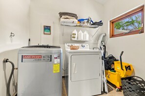 A laundry area with a front-loading washing machine, a dryer, and a small shelf with cleaning supplies. - Bubali Villa - Just a 2-minute drive to Eagle Beach (Eagle Beach)
