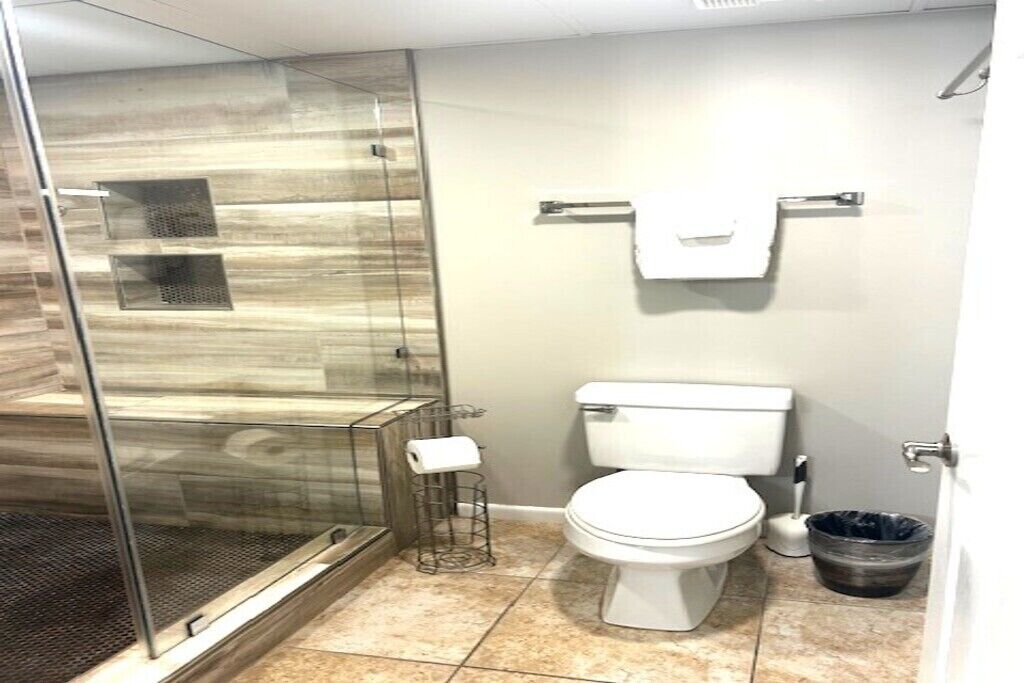 A bathroom with a glass-enclosed shower, a toilet, and a trash bin.