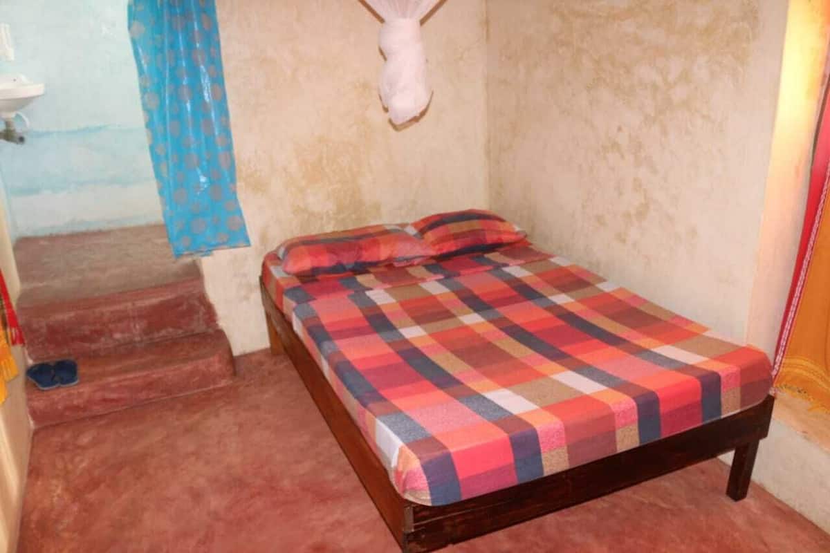 A small, single-bed room with a checkered bedspread, a blue curtain, and a white wall-mounted sculpture.
