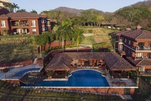Um resort com uma piscina grande, vários edifícios e uma paisagem acidentada ao fundo.