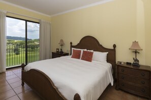 Quarto com uma cama grande, duas mesas de cabeceira e vista para uma paisagem verde através de uma porta de correr.