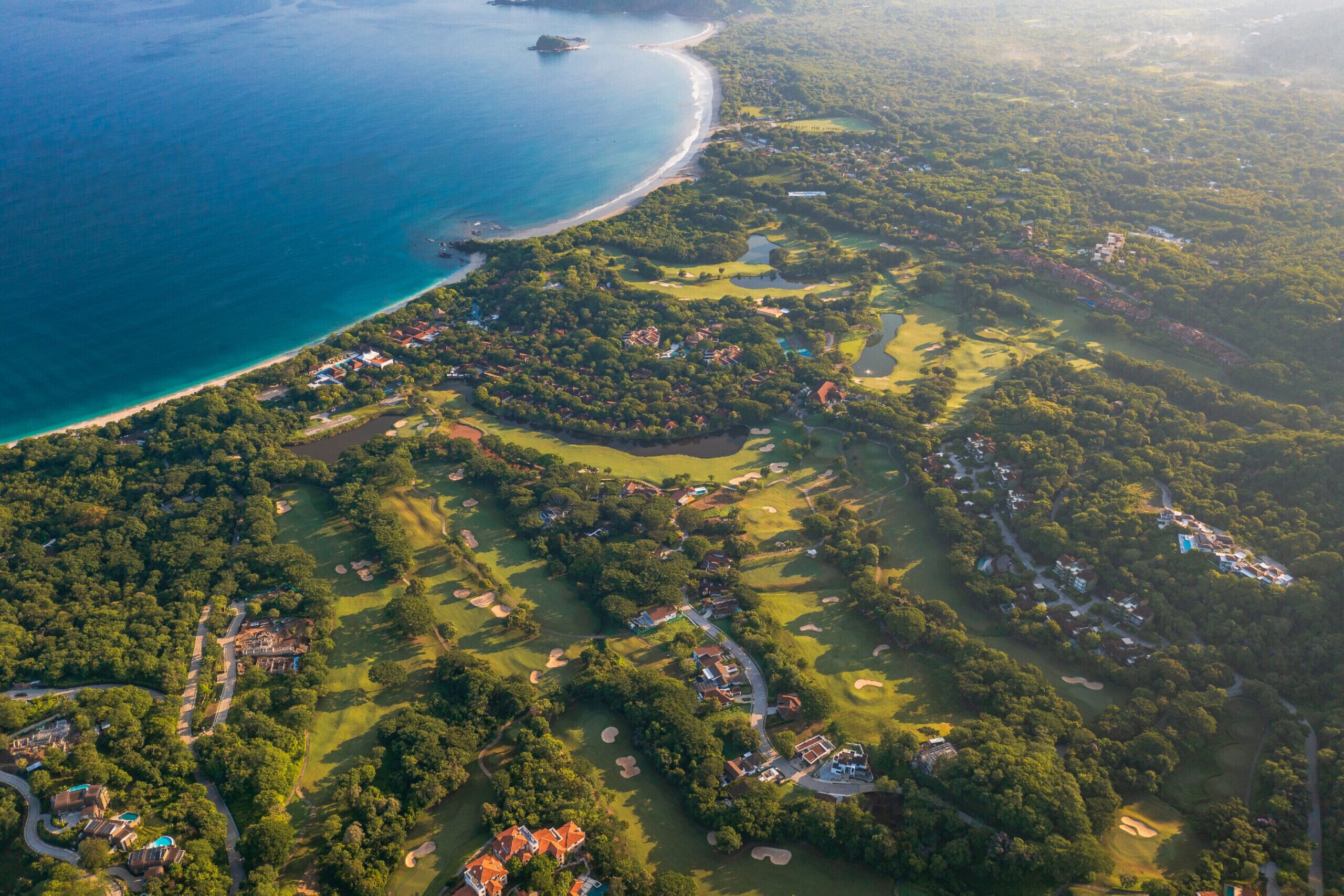 An aerial view of a coastal golf resort with multiple golf courses, a beach, and residential areas.