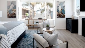 A modern bedroom with a large bed, a sofa, a small table with plants, and artwork on the walls. - Stylish 4BD/4BA • A/C • Private Rooftop Patio • Bikes • WiFi • 2-Car Parking! (Newport Beach)