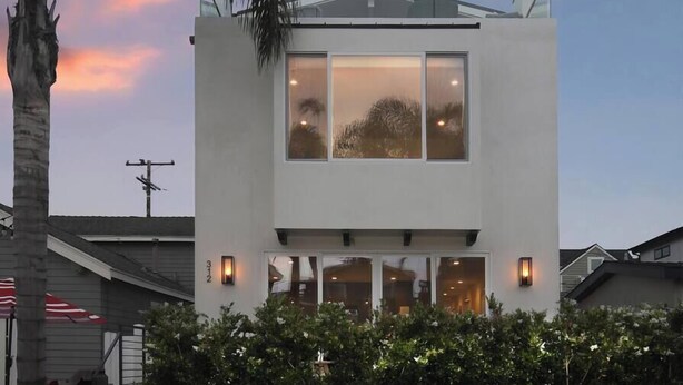 A modern two-story house with large windows, a flat roof, and a white exterior. - Stylish 4BD/4BA • A/C • Private Rooftop Patio • Bikes • WiFi • 2-Car Parking! (Newport Beach)