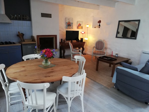 A cozy living room with a wooden dining table, white chairs, a sofa, and a TV.