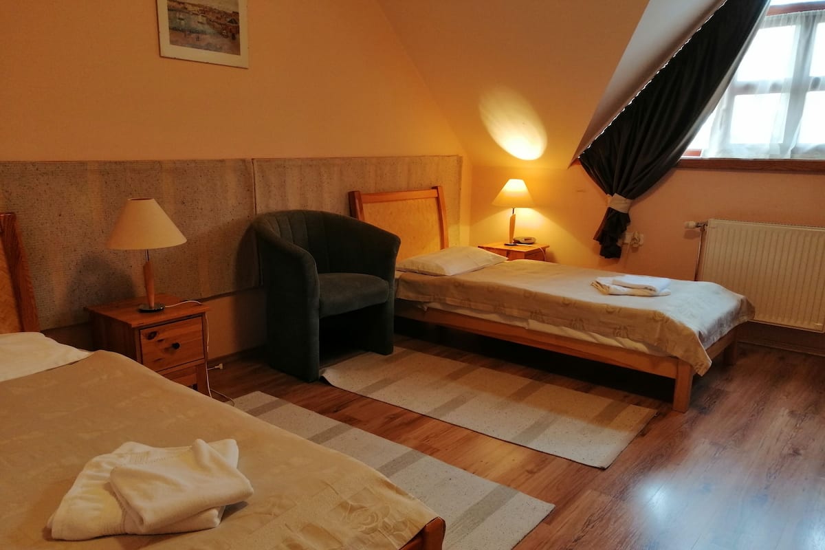 Una habitación de hotel con dos camas, una silla, una mesita de noche con lámpara y una ventana con cortinas.