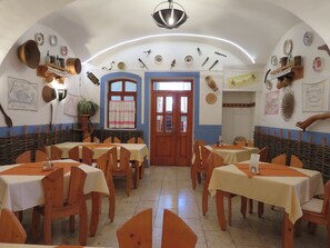 A traditional dining area with wooden tables and chairs, a central doorway, and decorative plates on the walls. - Józsi Bácsi Vendéglője és Szállodája (Szombathely)