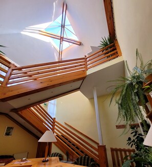 A multi-level wooden staircase with a skylight, indoor plants, and a sign indicating a location. - Józsi Bácsi Vendéglője és Szállodája (Szombathely)