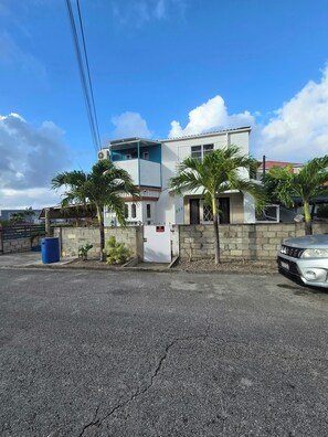 A residential building with a gated entrance, a parked car, and palm trees.