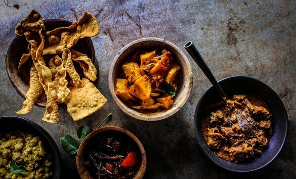 Variedad de platos, incluyendo un tazón que parece ser un curry de carne, un tazón de verduras y un tazón que parece una preparación de patatas, todo servido en una mesa rústica.