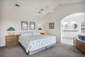 A bedroom with a bed, two bedside tables, a ceiling fan, and a bathroom with a sink and mirror.