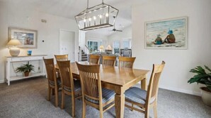 Un coin repas avec une table et des chaises en bois, un luminaire suspendu, un tableau au mur et un escalier en arrière-plan.