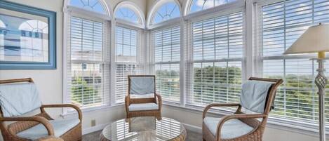 A sunroom with wicker furniture, large windows, and a view of the outdoors.