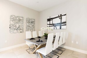 Un comedor con una mesa rectangular, sillas blancas y dos obras de arte abstracto en la pared.