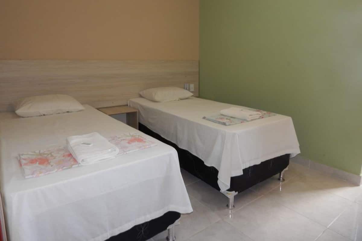 Ein Zimmer mit zwei Betten, jeweils mit weißer Bettdecke und Kissen, sowie einem kleinen Tisch mit einem Handtuch.