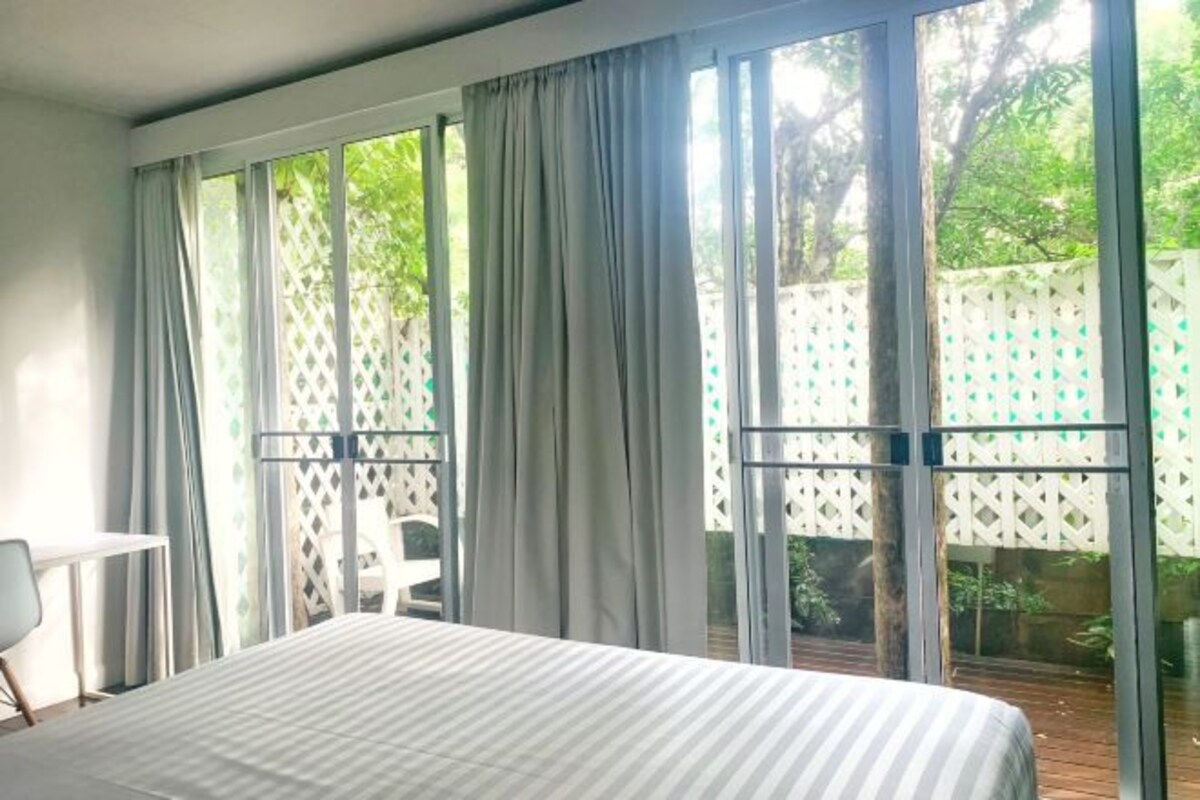 Une chambre avec une grande fenêtre, un lit, une chaise et une petite table.