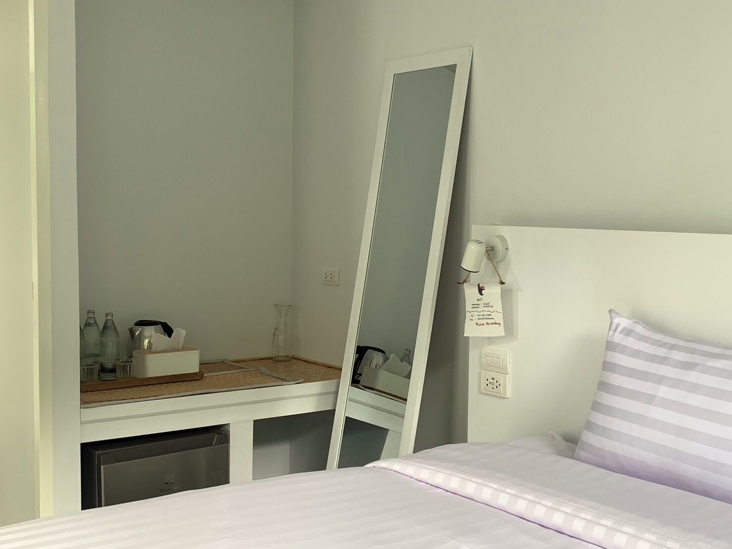 A bedroom with a bed, a bedside table with a lamp, a mirror, and a wall-mounted telephone.