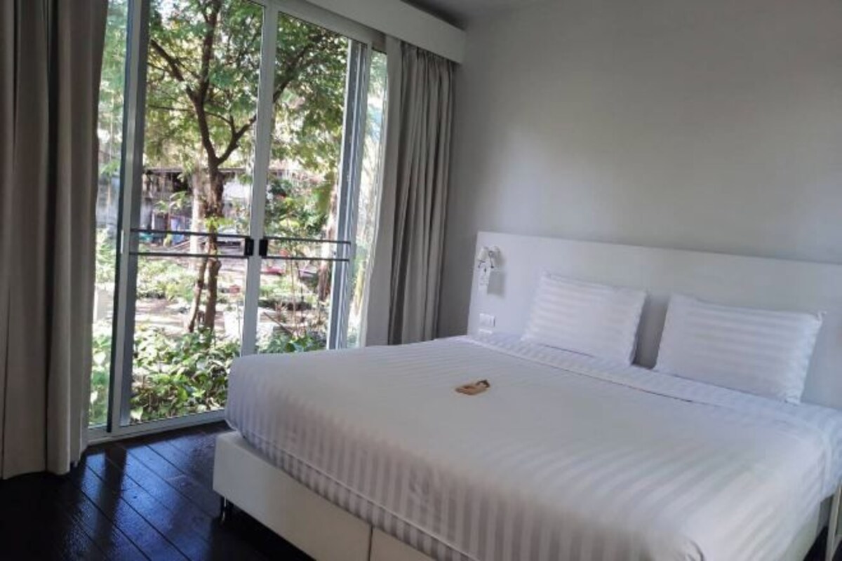 Une chambre avec un grand lit, une fenêtre avec des rideaux et une vue sur la verdure.