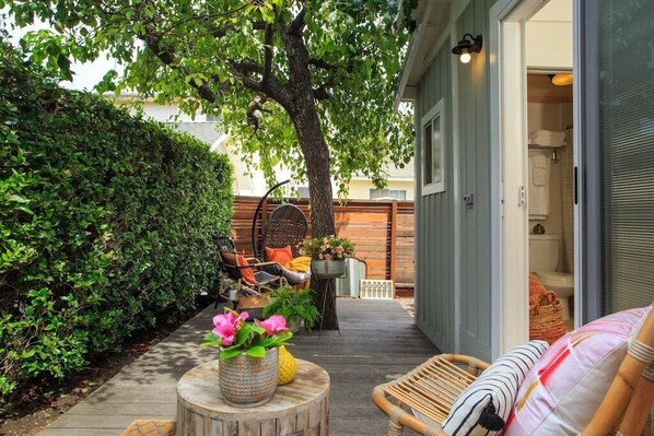 A cozy outdoor seating area with a wooden deck, wicker chairs, and a variety of potted plants.