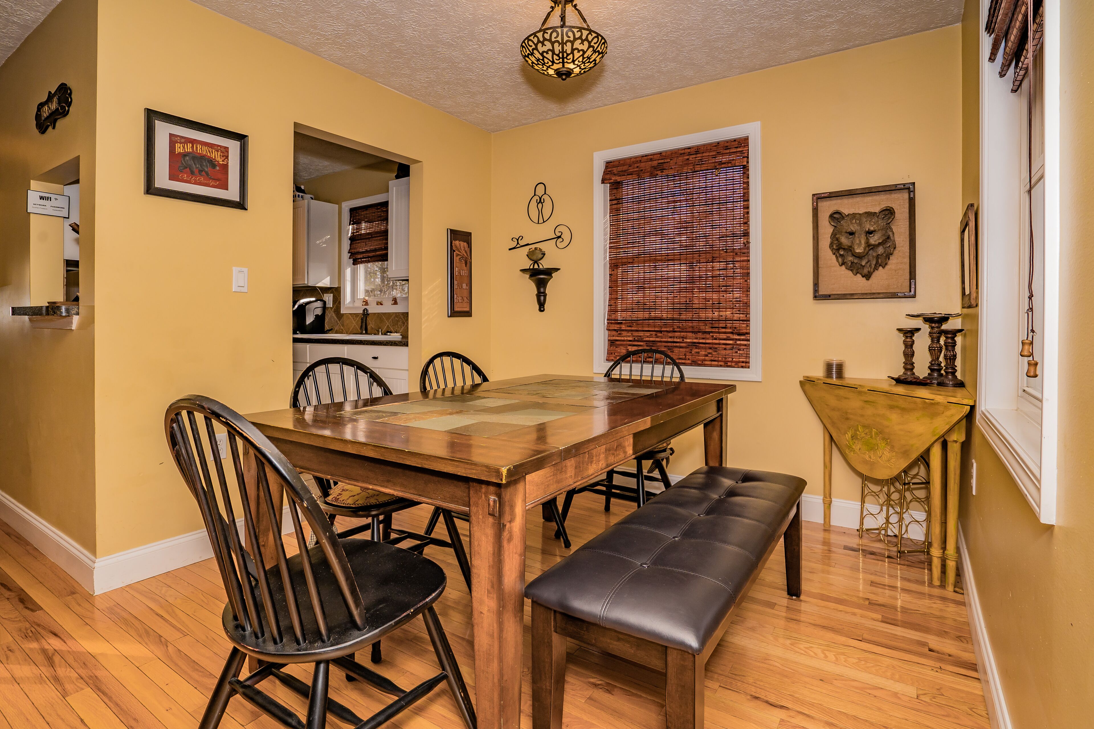 A dining area with a wooden table, four chairs, a bench, and a wall-mounted light fixture.