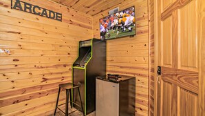 Une pièce aux murs lambrés, avec un téléviseur fixé au mur diffusant un match de football, un petit réfrigérateur et un coin bar avec un tabouret.