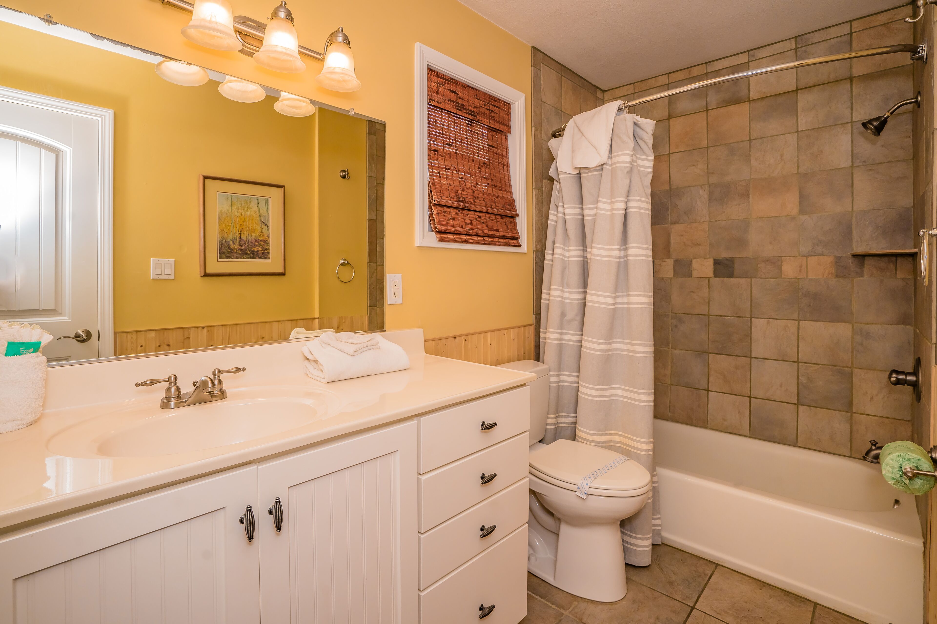 A bathroom with a white vanity, a toilet, a bathtub, and a shower curtain.