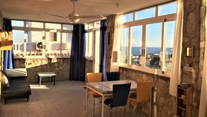 Un comedor con una mesa, sillas, un banco y vistas al mar a través de amplios ventanales.