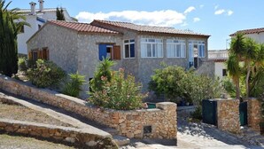 Una casa de piedra con tejado de tejas, una escalera de piedra y un jardín con diversas plantas y flores.