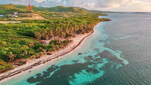 An aerial view of a coastal area with a beach, dense vegetation, and a distant structure. - Villa entre Ciel et Mer (Sainte-Anne)