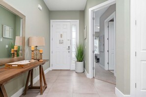 A hallway with a wooden console table, two lamps, a potted plant, and a white door.