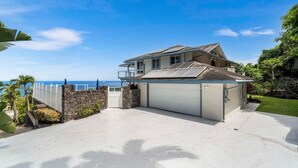 Une maison à deux étages avec un garage, un mur en pierre et une vue sur l’océan.