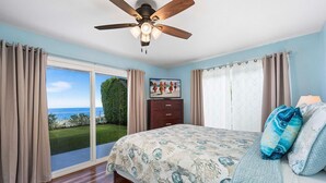 Une chambre avec un lit, un ventilateur de plafond, une télévision et une vue sur l’océan.