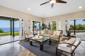 A spacious living room with a large glass coffee table, beige sofas, and a view of the ocean.