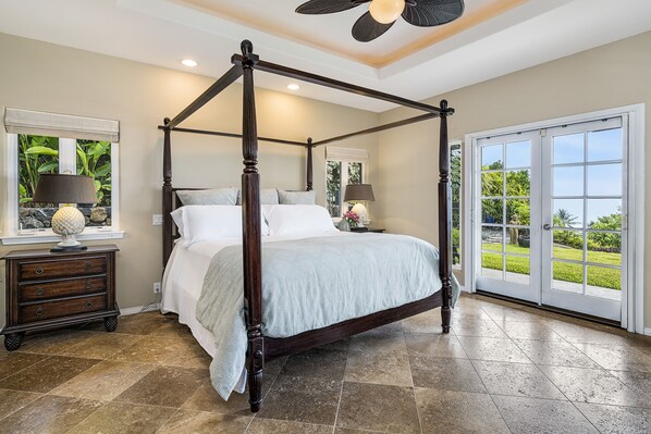 A four-poster bed with a view of the outdoors through a large sliding glass door.