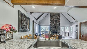 A kitchen with a granite countertop, stainless steel sink, wooden chairs, and a stone fireplace.