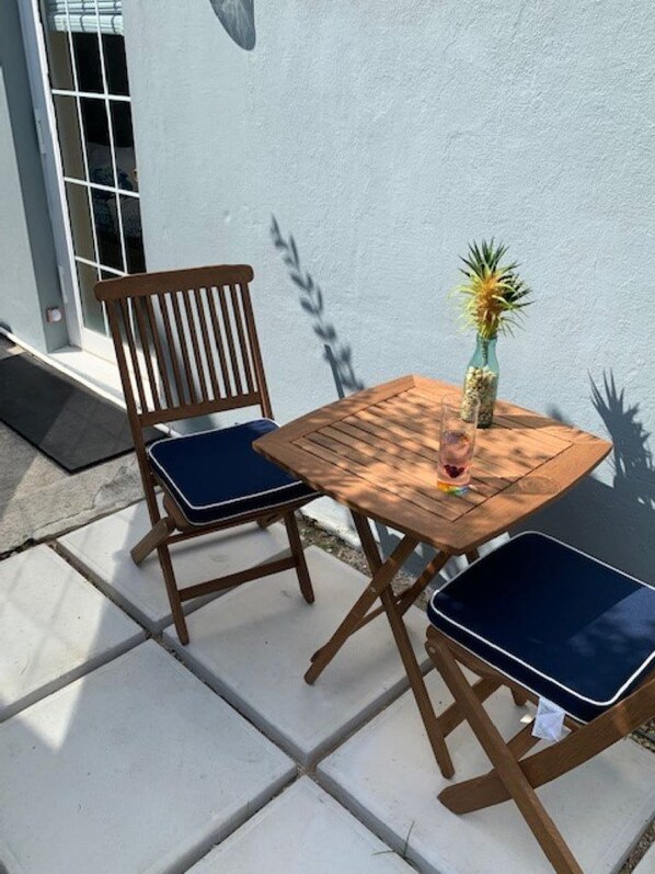 Une table en bois et deux chaises avec des coussins bleus, un ananas dans un vase et une ombre sur le mur.