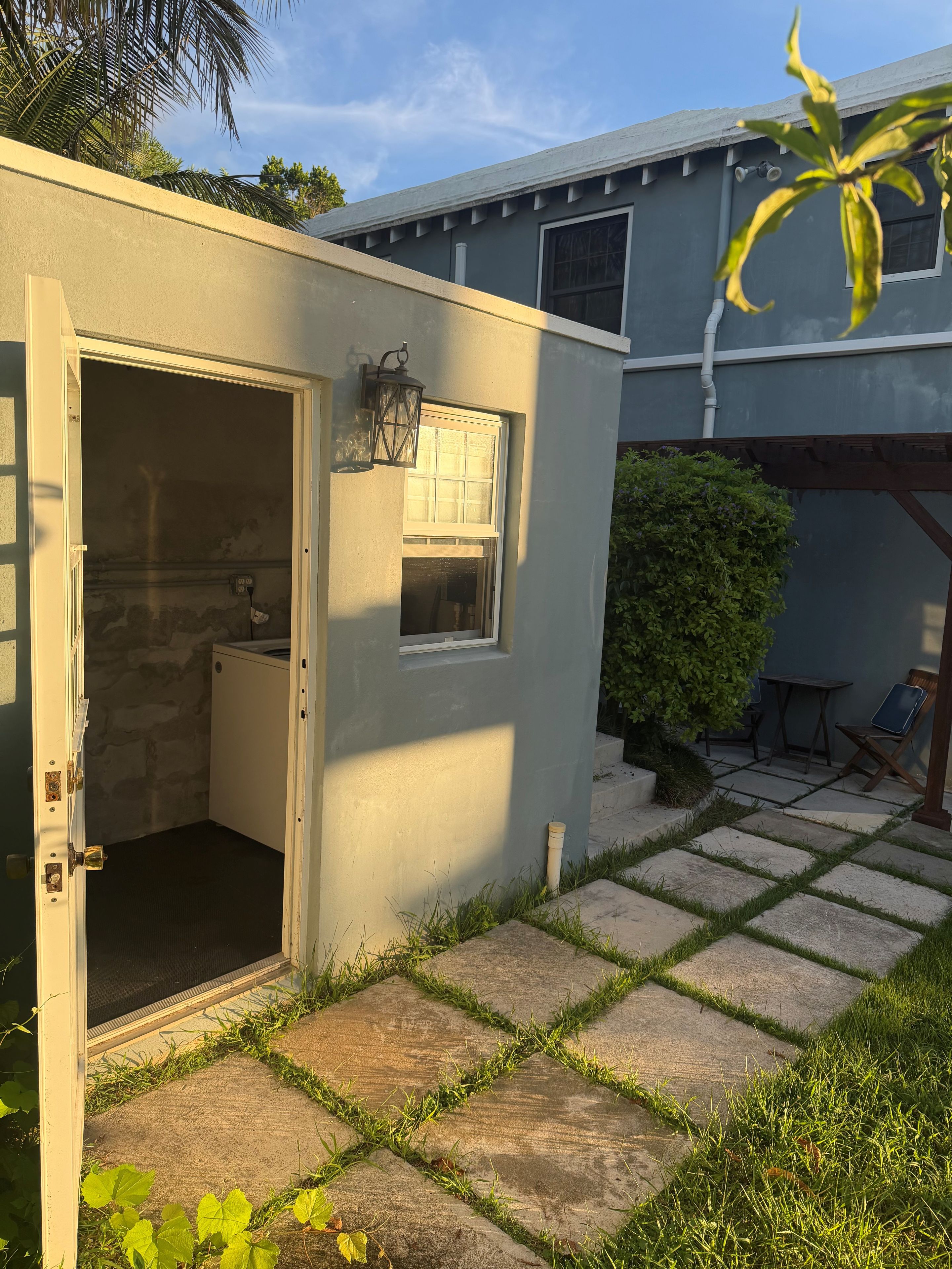 A small, enclosed outdoor area with a door leading to a screened-in space, a window, and a concrete pathway with grass edging.