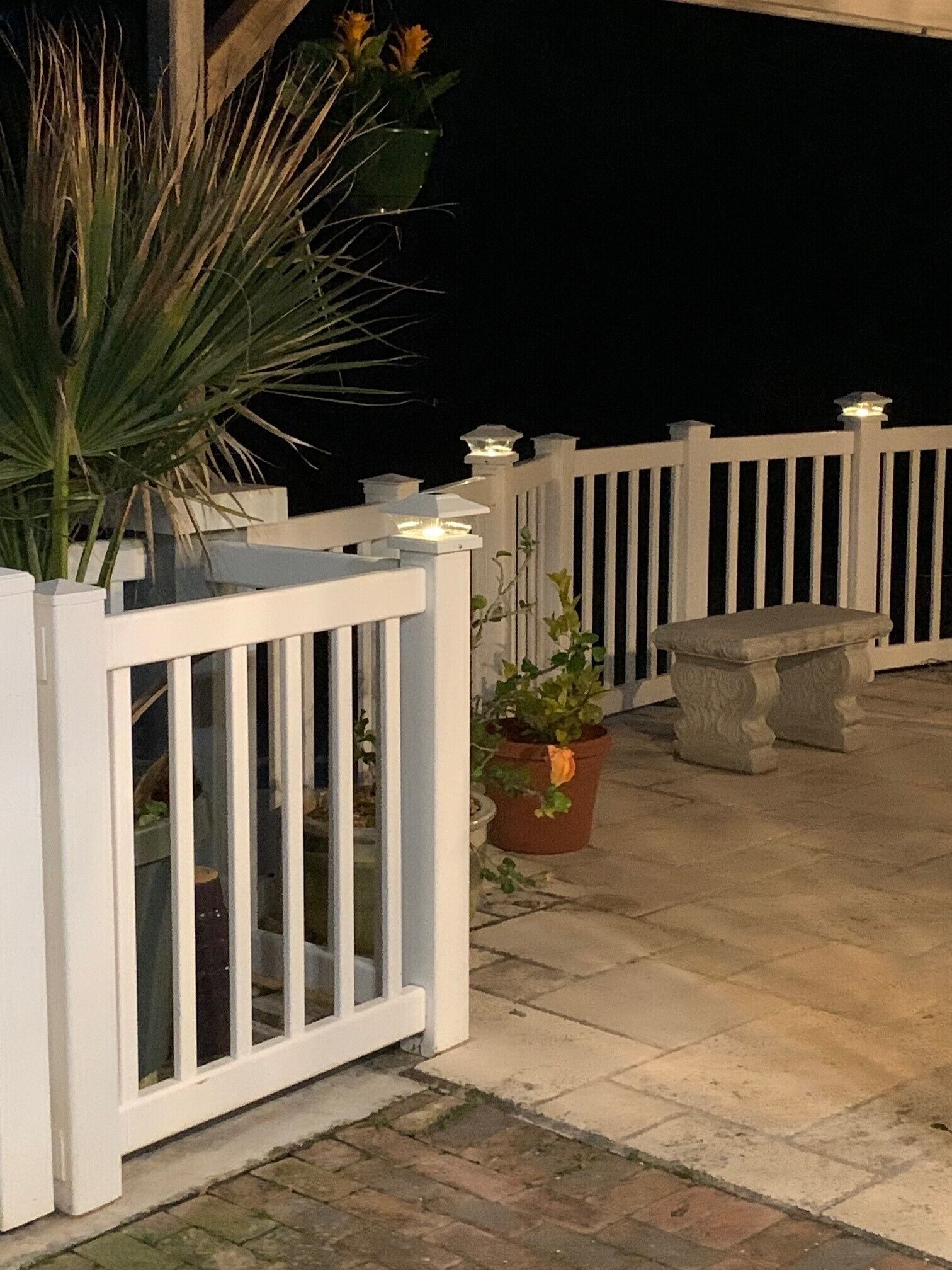 A covered outdoor area with a white railing, potted plants, and a stone bench.