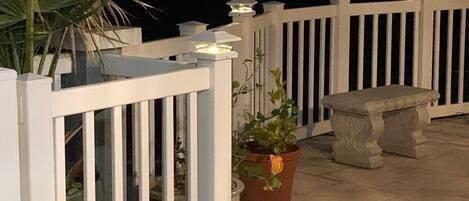 A covered outdoor area with a white railing, potted plants, and a stone bench.