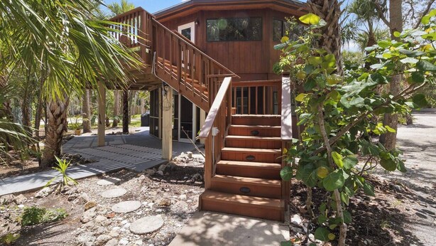A wooden cabin with a staircase leading to a deck, surrounded by trees and a rocky ground. - Boaters Paradise W Dock Access - .4 Mile to Beach (Englewood)