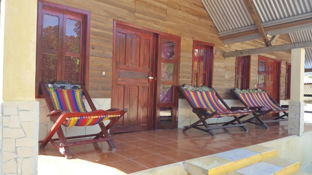 Un edificio de madera con un porche cubierto, dos puertas de madera y dos sillones coloridos.