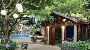 Eine Terrasse mit einer Steinsäule, einer kleinen Holzhütte mit Ziegeldach, Sitzgelegenheiten im Freien und einem Pool.
