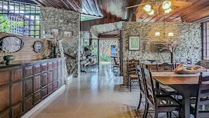 Ein geräumiger, gut beleuchteter Innenraum mit Steinwand, Holzboden und einem zentral gelegenen Essbereich mit Stühlen und Tisch.