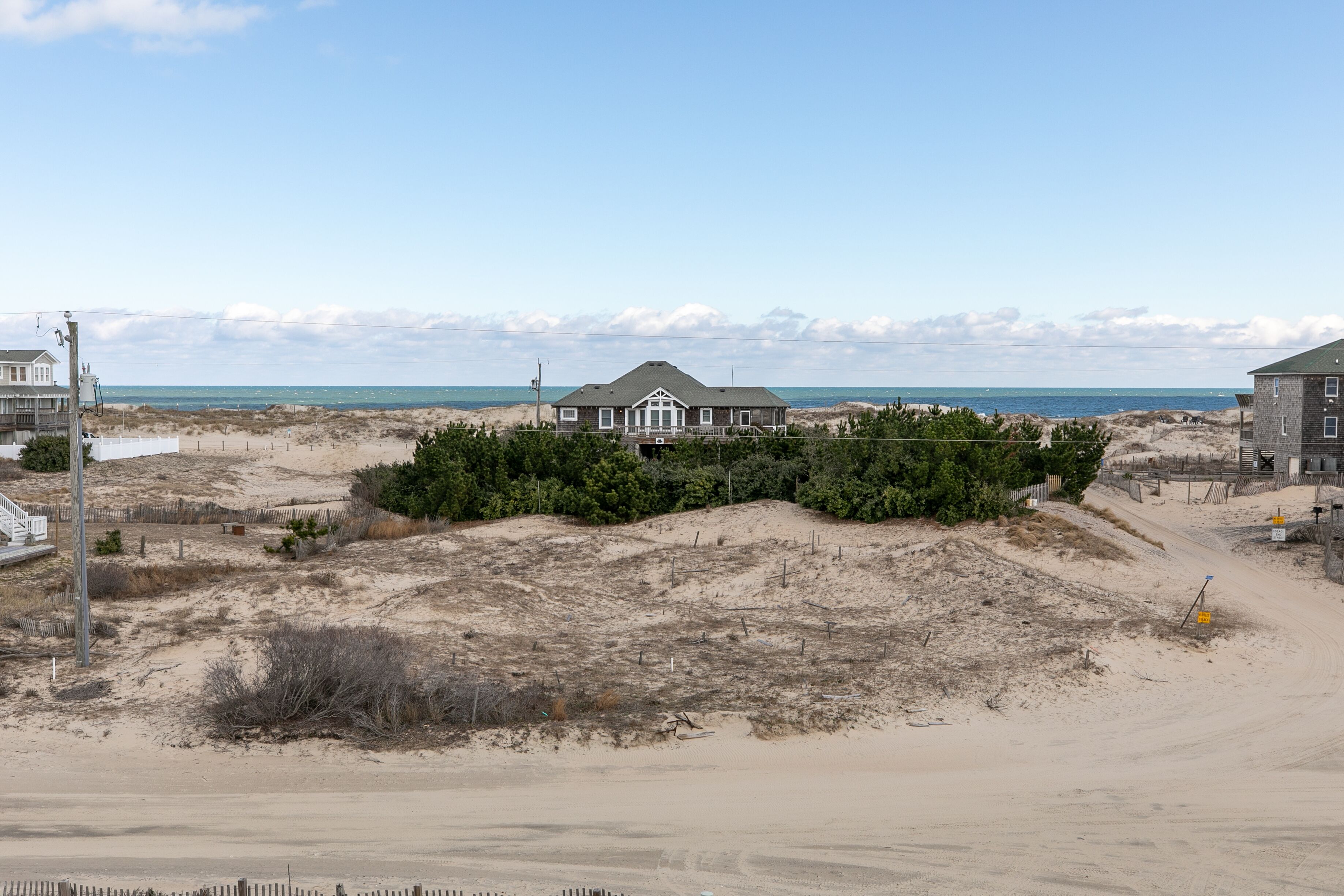 A beachfront property with a large house, sandy dunes, and a clear view of the ocean.
