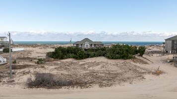 A beachfront property with a large house, sandy dunes, and a clear view of the ocean.